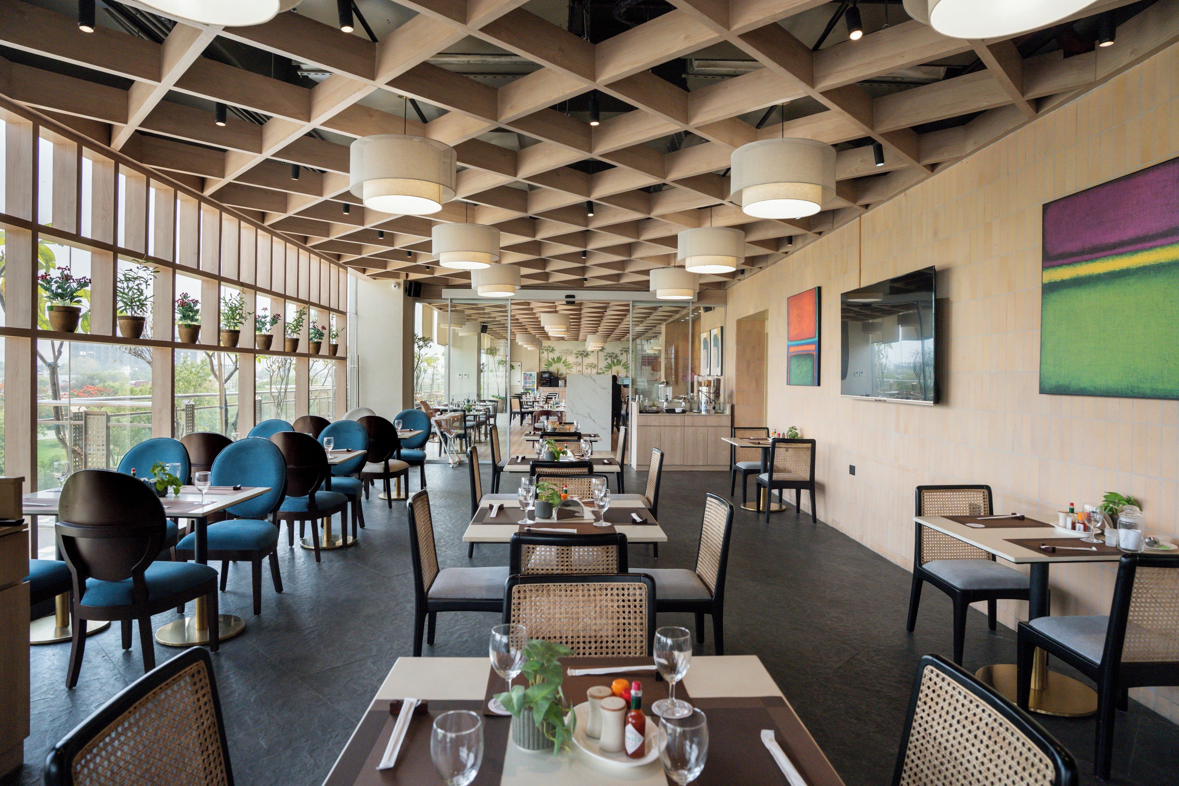 Un restaurante espacioso con un diseño moderno, que presenta un techo con diseño de cuadrícula, ventanas amplias y diferentes opciones de asientos.