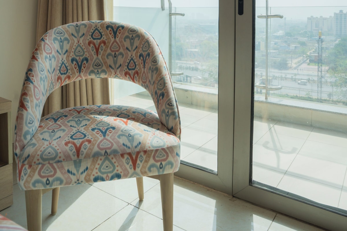 Ein Zimmer mit einem gemusterten Sessel, einer Schiebetür aus Glas und Blick auf eine Stadtansicht.