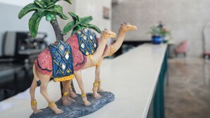 A reception desk with two camel figurines, a modern chandelier, and a large abstract painting on the wall. - AR Suites KLJ Square (Gurugram)