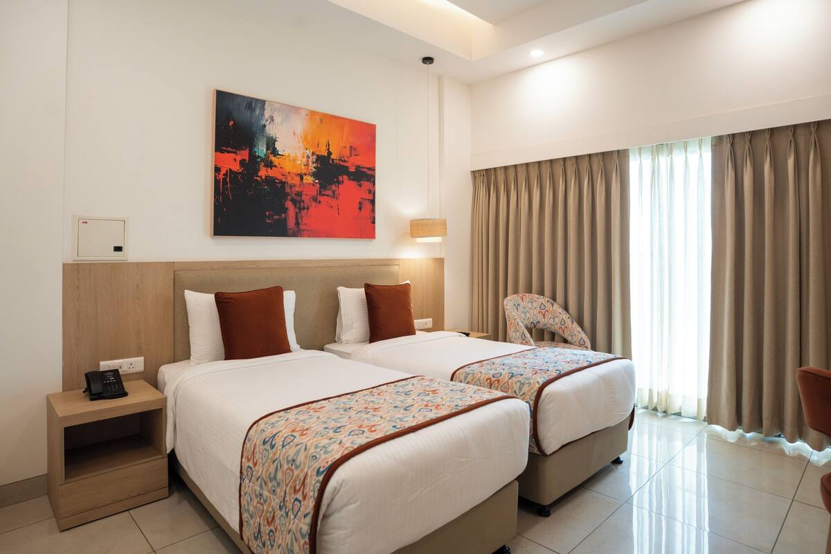 A hotel room with two beds, a nightstand with a phone, a painting on the wall, and a window with curtains.