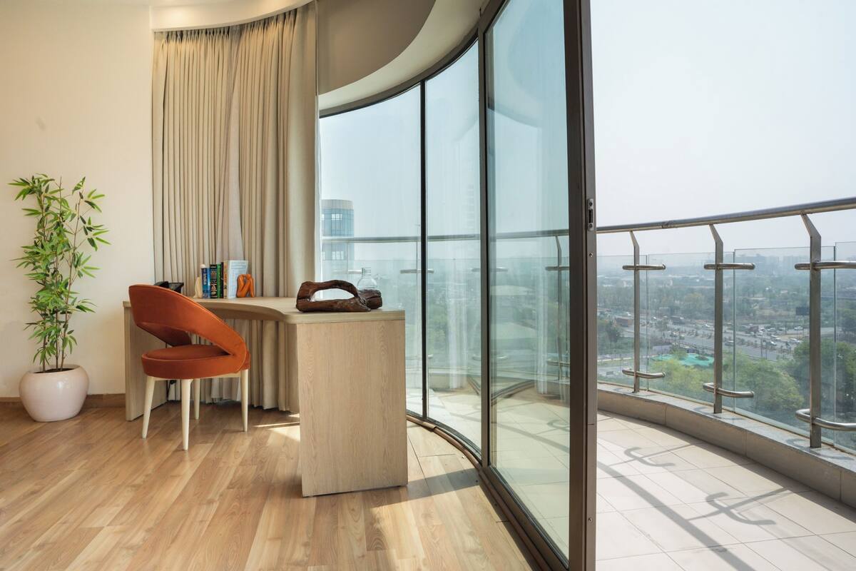 A modern room with a curved glass balcony, a wooden desk, a chair, and a potted plant.
