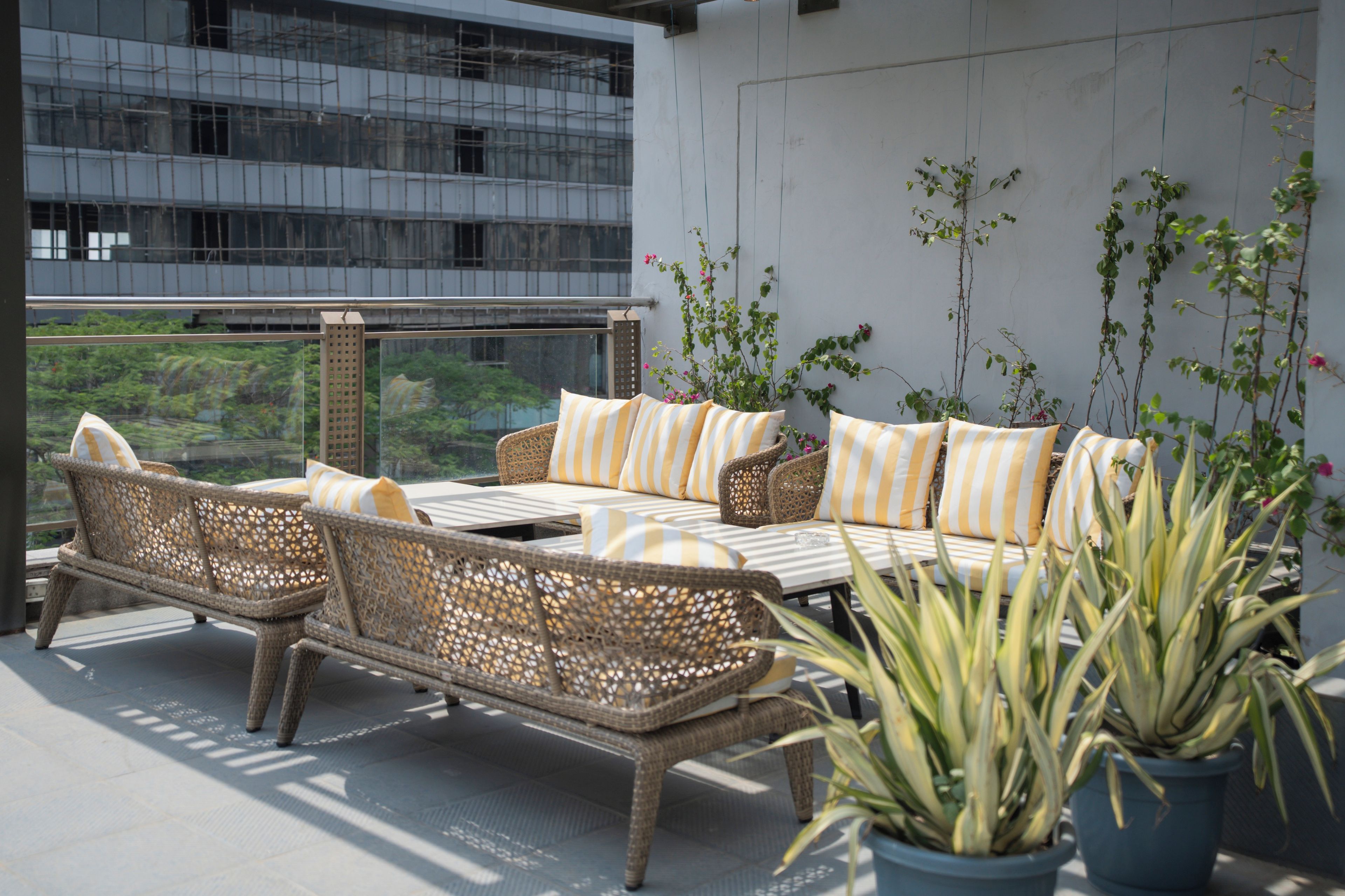 Un balcon agrémenté de meubles en osier, de plantes en pot et offrant une vue sur un immeuble moderne.