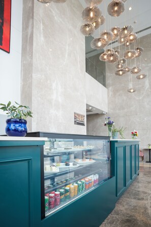 A modern interior with a teal counter, a glass display case with beverages, and hanging spherical light fixtures. - AR Suites KLJ Square (Gurugram)