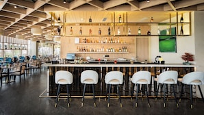 A modern bar area with a wooden ceiling, multiple shelves of liquor bottles, and bar stools. - AR Suites KLJ Square (Gurugram)