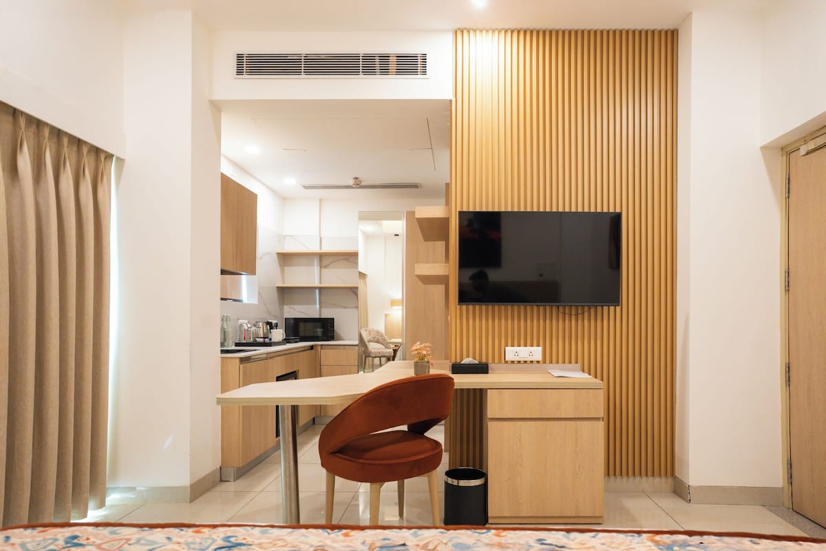 Ein modernes Zimmer mit Schreibtisch aus Holz, einem an der Wand befestigten Fernseher, einem Stuhl und einer kleinen Mülltonne.