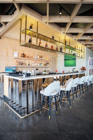 A modern bar area with a long counter, multiple shelves of bottles, and white bar stools. - AR Suites KLJ Square (Gurugram)
