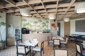 Un restaurant avec un plafond en bois, une fresque représentant des palmiers et un comptoir équipé d’un ordinateur. Des tables et des chaises sont disposées pour accueillir les clients.