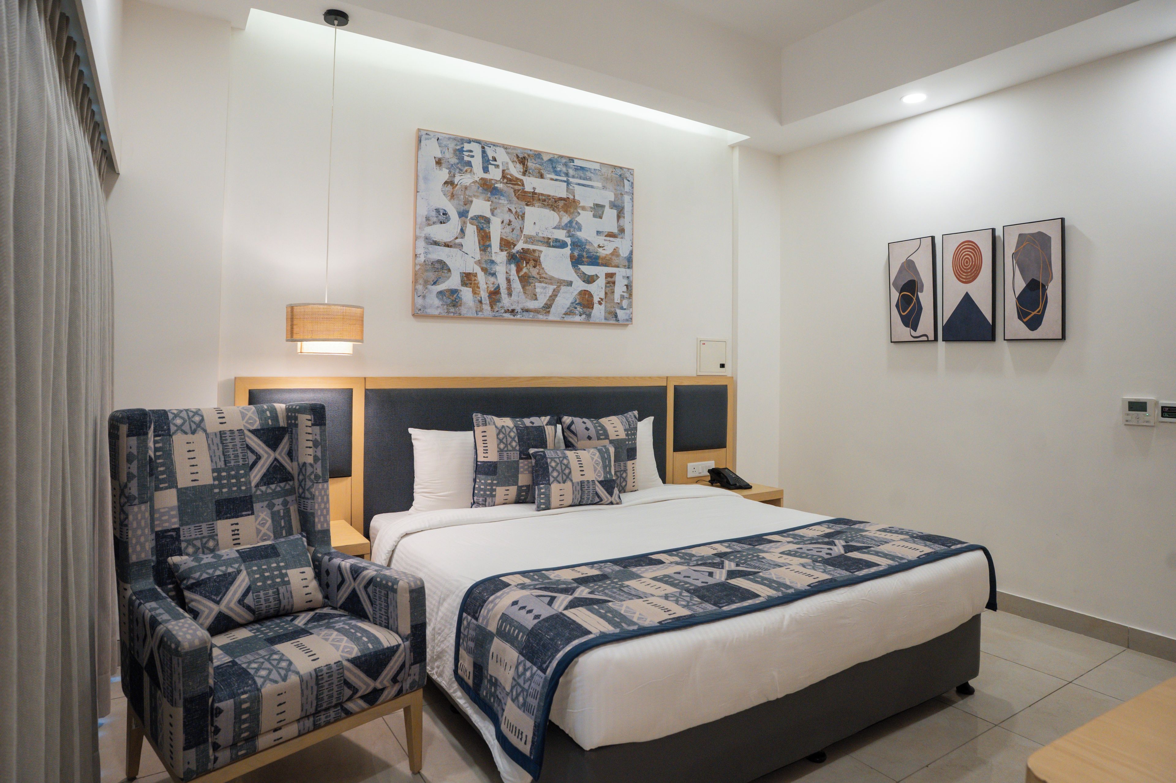 Una habitación de hotel con una cama, dos sillones, una mesita de noche y una obra de arte colgada en la pared.