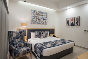 A hotel room with a bed, two armchairs, a nightstand, and a wall-mounted artwork. - AR Suites KLJ Square (Gurugram)