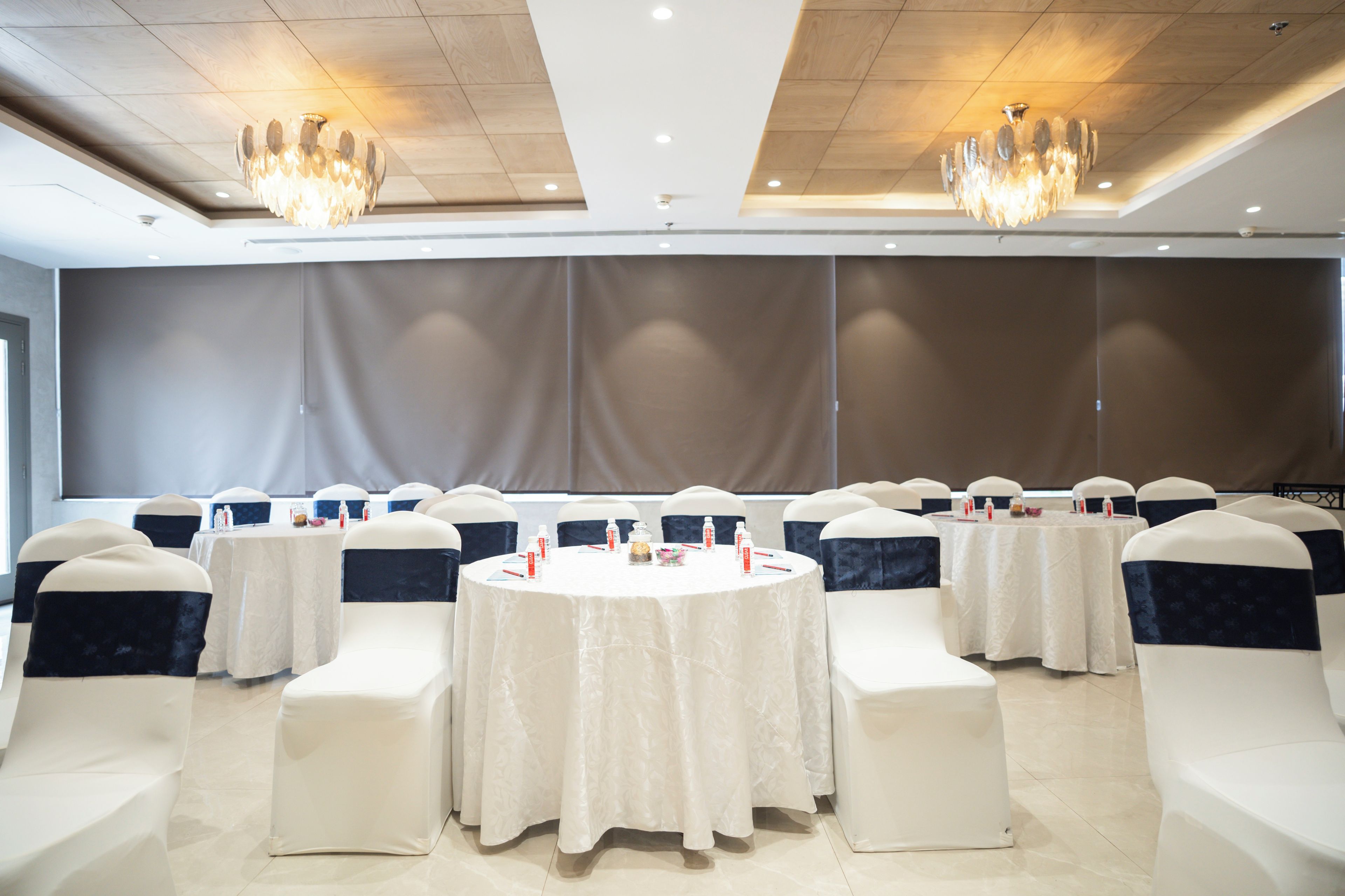 Un salón de conferencias con mesas redondas, sillas blancas con cintas oscuras y candelabros.