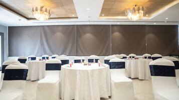 Un salón de conferencias con mesas redondas, sillas blancas con cintas oscuras y candelabros.