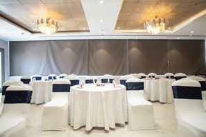 A conference room with round tables, white chairs with dark sashes, and chandeliers. - AR Suites KLJ Square (Gurugram)