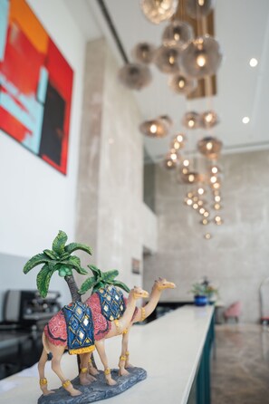 A reception desk with two camel figurines, a modern chandelier, and a large abstract painting on the wall. - AR Suites KLJ Square (Gurugram)