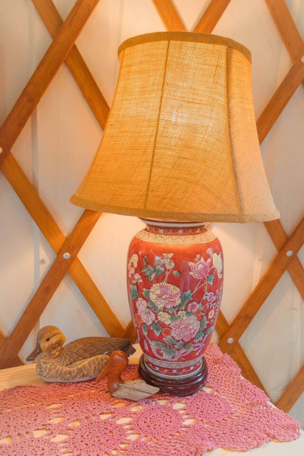 A lamp with a woven shade on a table with a pink crocheted placemat.