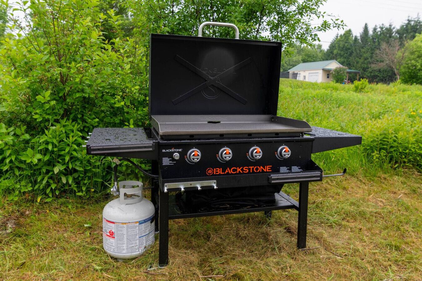 A black outdoor grill with three control knobs and a propane tank.