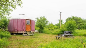 A yurt with a wooden door and steps, a picnic table, and a grill in a grassy area with trees. - Farm Stay Yurt - 7 min St Albans (Fairfield)