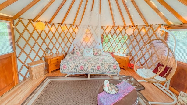 A cozy interior of a yurt with a bed, a hanging chair, and a small table with a cup. - Farm Stay Yurt - 7 min St Albans (Fairfield)