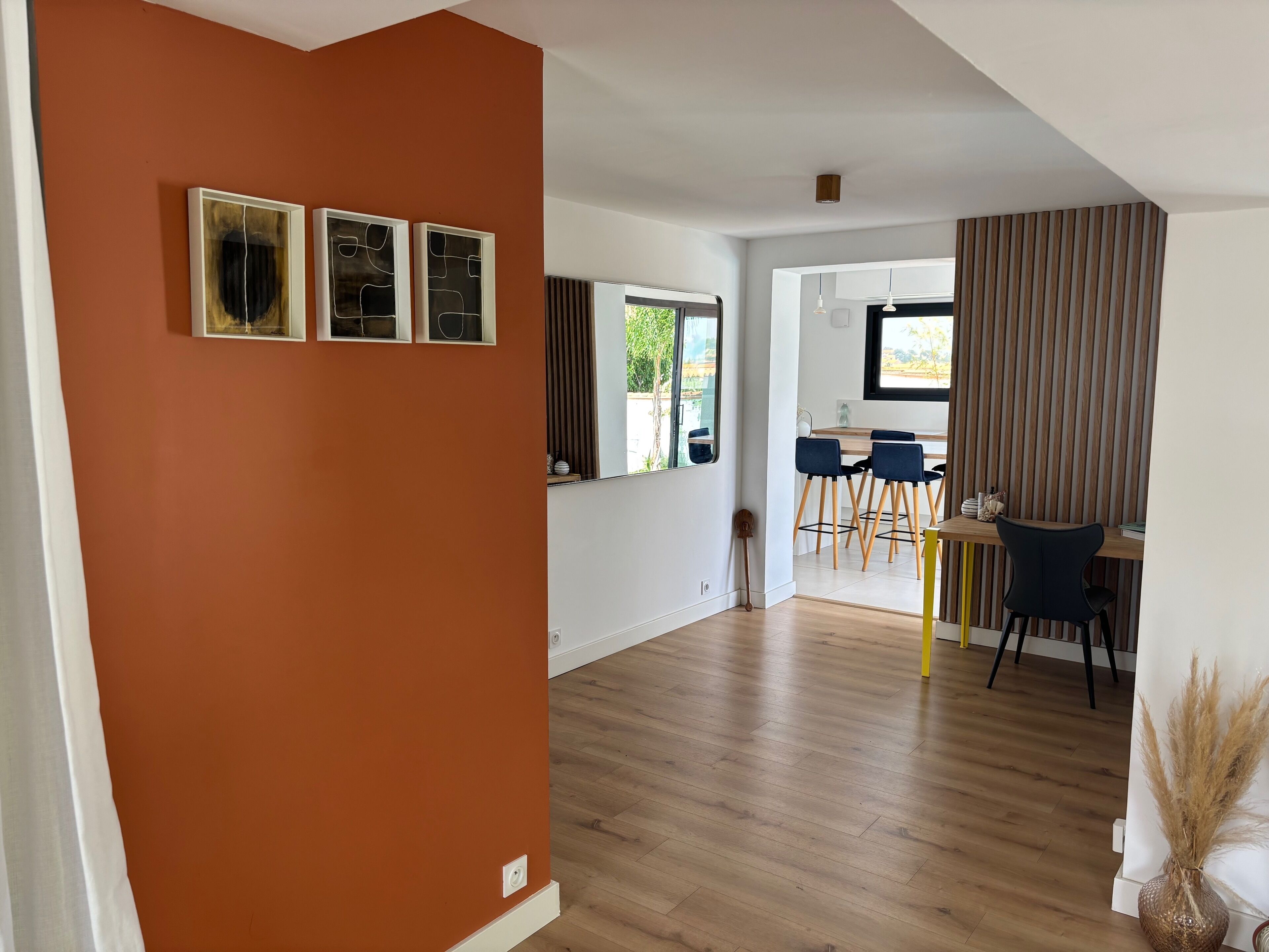 A spacious room with a wooden floor, a dining area with a table and chairs, and a window with blinds.