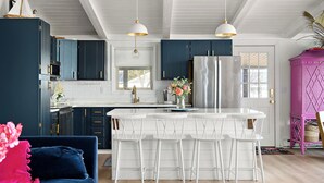Una cocina moderna con armarios azul oscuro, una isla blanca con taburetes, y un mueble rosa.