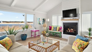 Amplia sala de estar con chimenea, ventanas grandes y vista a la playa.
