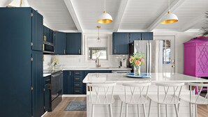 Una cocina moderna con armarios azul oscuro, encimeras blancas y una isla central con taburetes de bar.