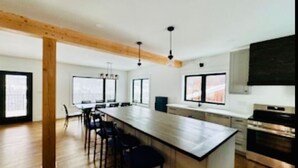 A modern kitchen with a large island, wooden beams, and a dining area with chairs.