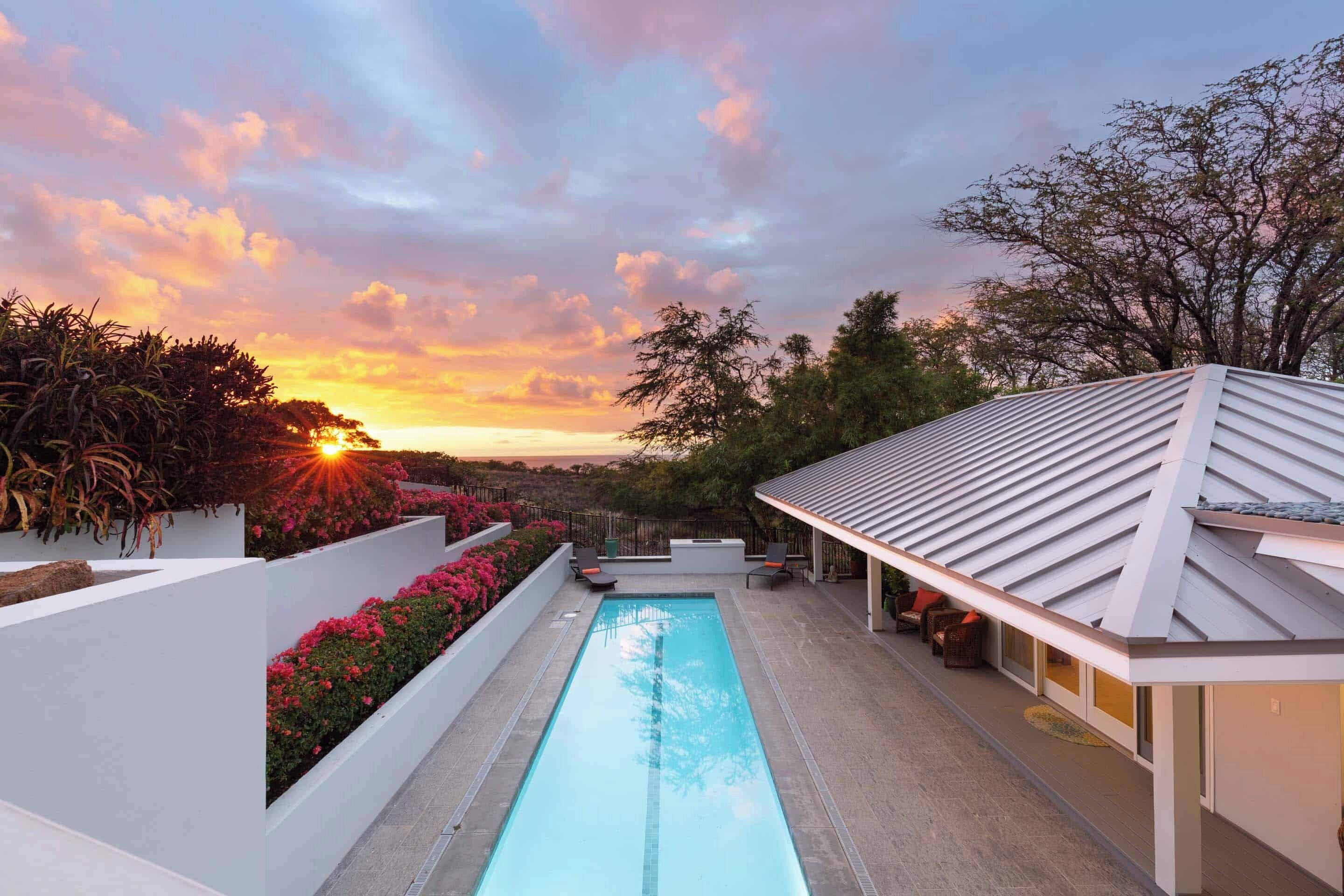 A swimming pool with a view of the sunset, surrounded by white walls and red flowers.