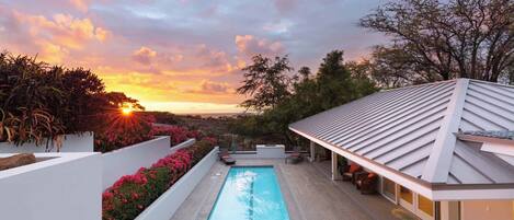 A swimming pool with a view of the sunset, surrounded by white walls and red flowers.