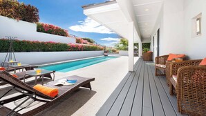 Un espace aménagé au bord de la piscine, avec des chaises longues, une piscine et un mur blanc agrémenté de verdure.