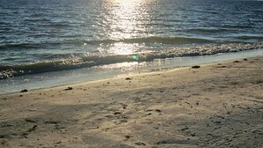 Una playa con el sol reflejándose en el agua, cielo despejado y un horizonte lejano.