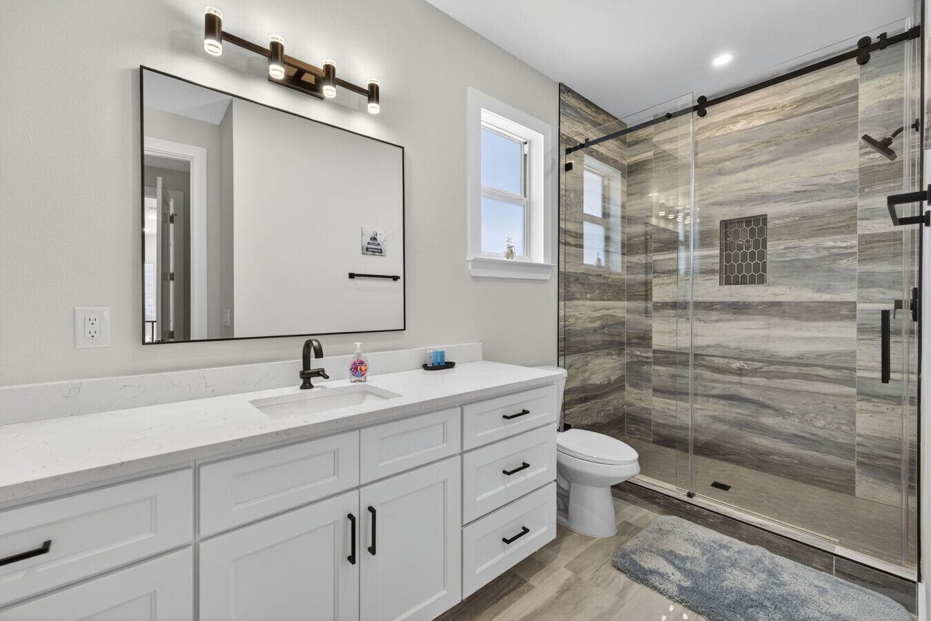 A modern bathroom with a large mirror, a white vanity, a glass shower enclosure, and a white toilet.