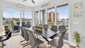 Un comedor con una mesa y sillas, un ventilador de techo y vistas a la playa y edificios.