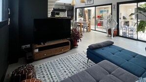 Ein modernes Wohnzimmer mit einem großen Flachbildfernseher, einem blauen Sofa und einem Essbereich im Hintergrund.