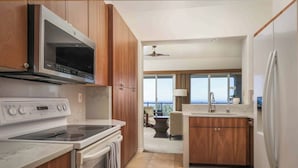 A modern kitchen with wooden cabinets, a built-in microwave, a stove, and a refrigerator. - Kumulani H3 Two Bedroom (Kamuela)