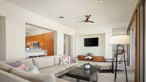 A modern living room with a sectional sofa, a coffee table, a TV, and a ceiling fan. - Kumulani H3 Two Bedroom (Kamuela)