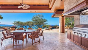 Une terrasse extérieure avec une table ronde et des chaises, un barbecue et une vue sur l’océan.