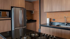 A modern kitchen with wooden cabinets, a stainless steel refrigerator, a black countertop, and a built-in microwave. - Apartment with Beautiful Views | ACASO 502 (Heroica Puebla de Zaragoza)