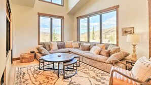 A spacious living room with a large sectional sofa, a round coffee table, and a view of the mountains through large windows.