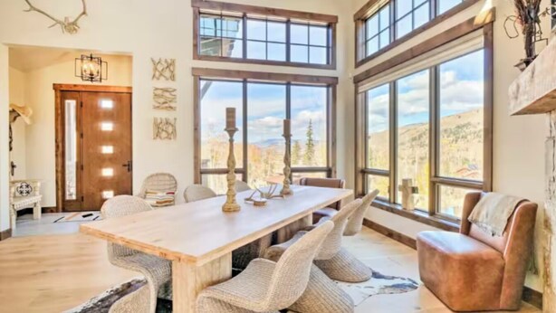 A spacious dining area with a long wooden table, woven chairs, and large windows offering a view of the outdoors.