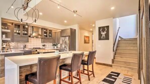 A modern kitchen with a central island, dark chairs, and a staircase leading to a second floor.