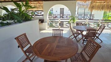 An outdoor patio with a round wooden table and chairs, a ceiling fan, and a view of a building through an arched doorway.