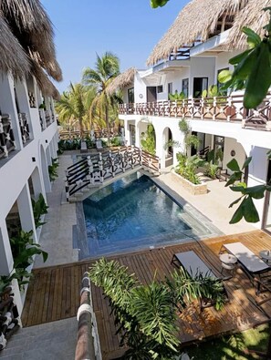 A resort with a swimming pool, wooden deck, and thatched-roof buildings. - To complete (El Paredon)