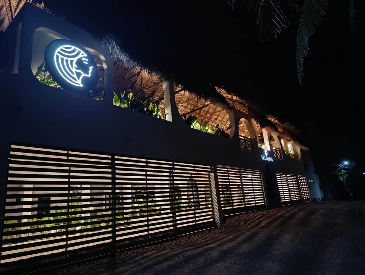 Un bâtiment à l’architecture moderne, doté d’un grand logo illuminé sur la façade et d’une toiture en chaume.