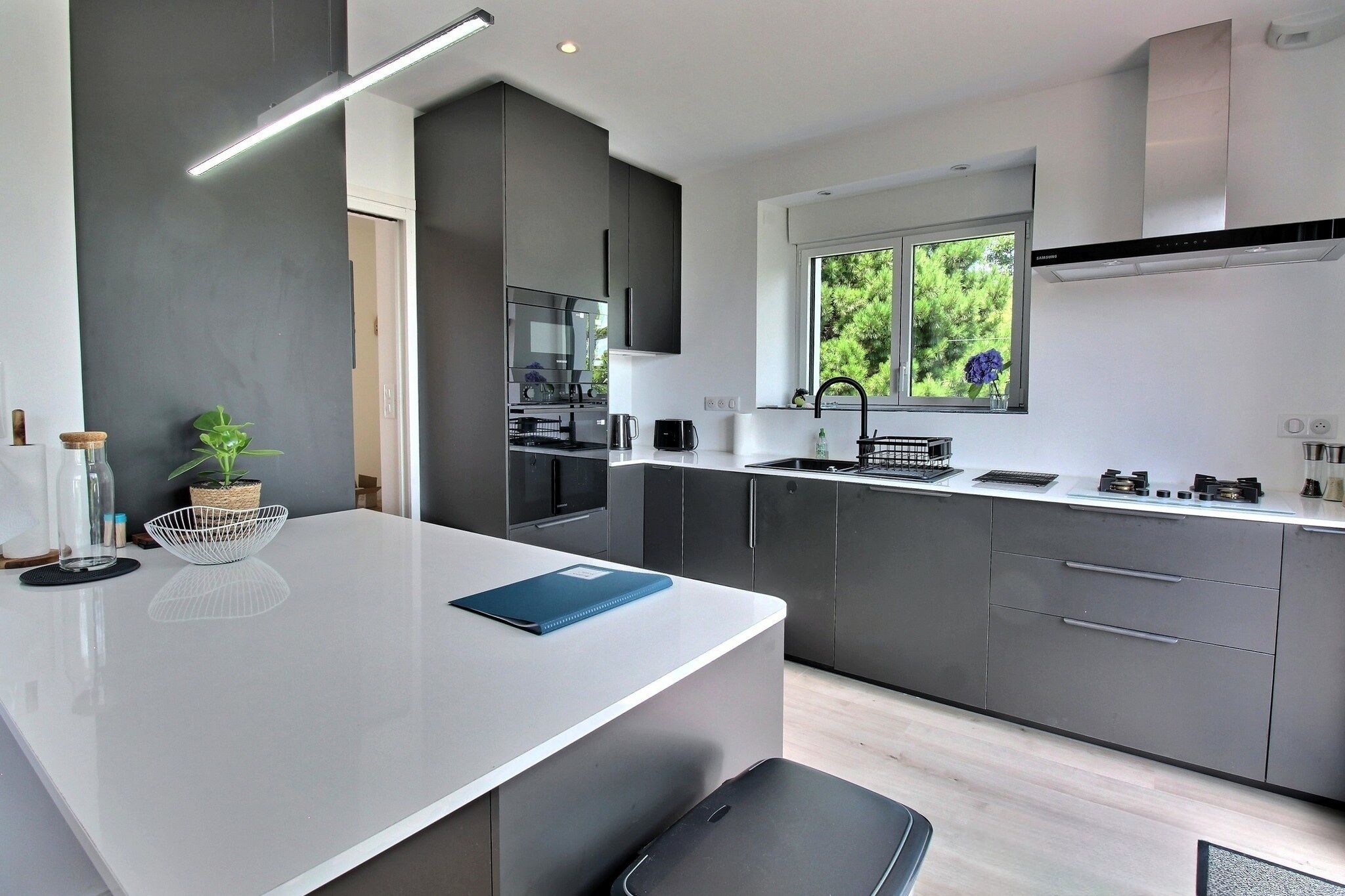 Una cocina moderna con una isla central, muebles oscuros y un ventanal con vistas a zonas verdes.