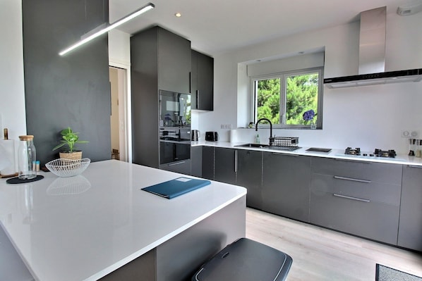 Una cocina moderna con una isla central, muebles oscuros y un ventanal con vistas a zonas verdes.