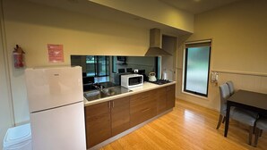 Une cuisine compacte équipée d’un réfrigérateur, d’un four à micro-ondes, d’une cuisinière et d’un évier. On y trouve une table à manger avec des chaises et une fenêtre à vitre dépolie.