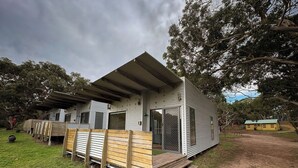Une maison mobile de plain-pied, dotée d’un toit plat, d’une terrasse en bois et d’un espace clôturé comprenant un petit abri de jardin.