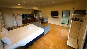 A compact hotel room with a bed, a small kitchenette, a seating area, and a TV. - DE 3 - Deluxe Open Plan Cabin (Cape Otway)