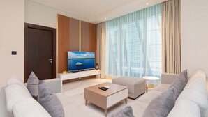 A modern living room with a flat-screen TV, a sofa, a coffee table, and a large window with curtains. - Stunning Corner Suite Canal View (Dubai)