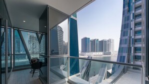 A modern hotel room with large floor-to-ceiling windows, a glass railing, and a view of the city skyline and water. - Stunning Corner Suite Canal View (Dubai)